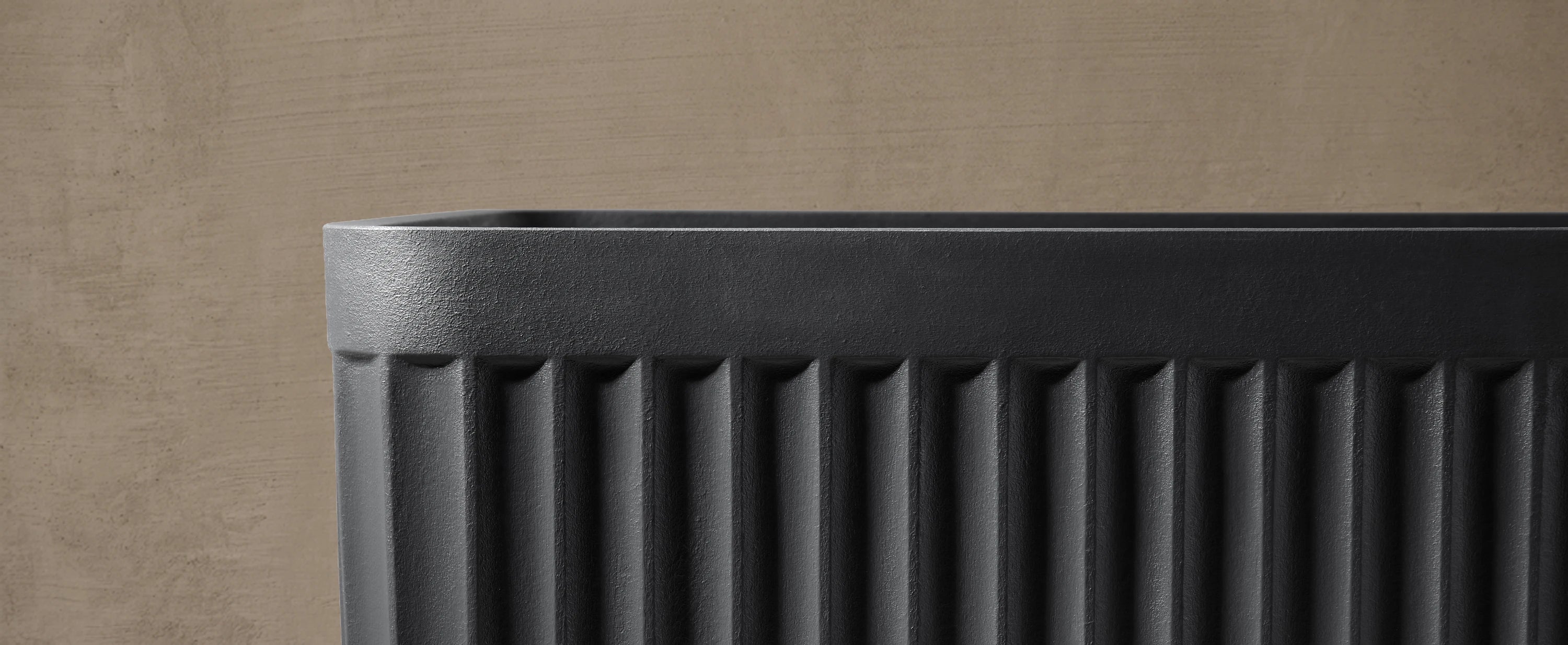 Close-up of the black KOLPA freestanding bath, against a taupe concrete wall.