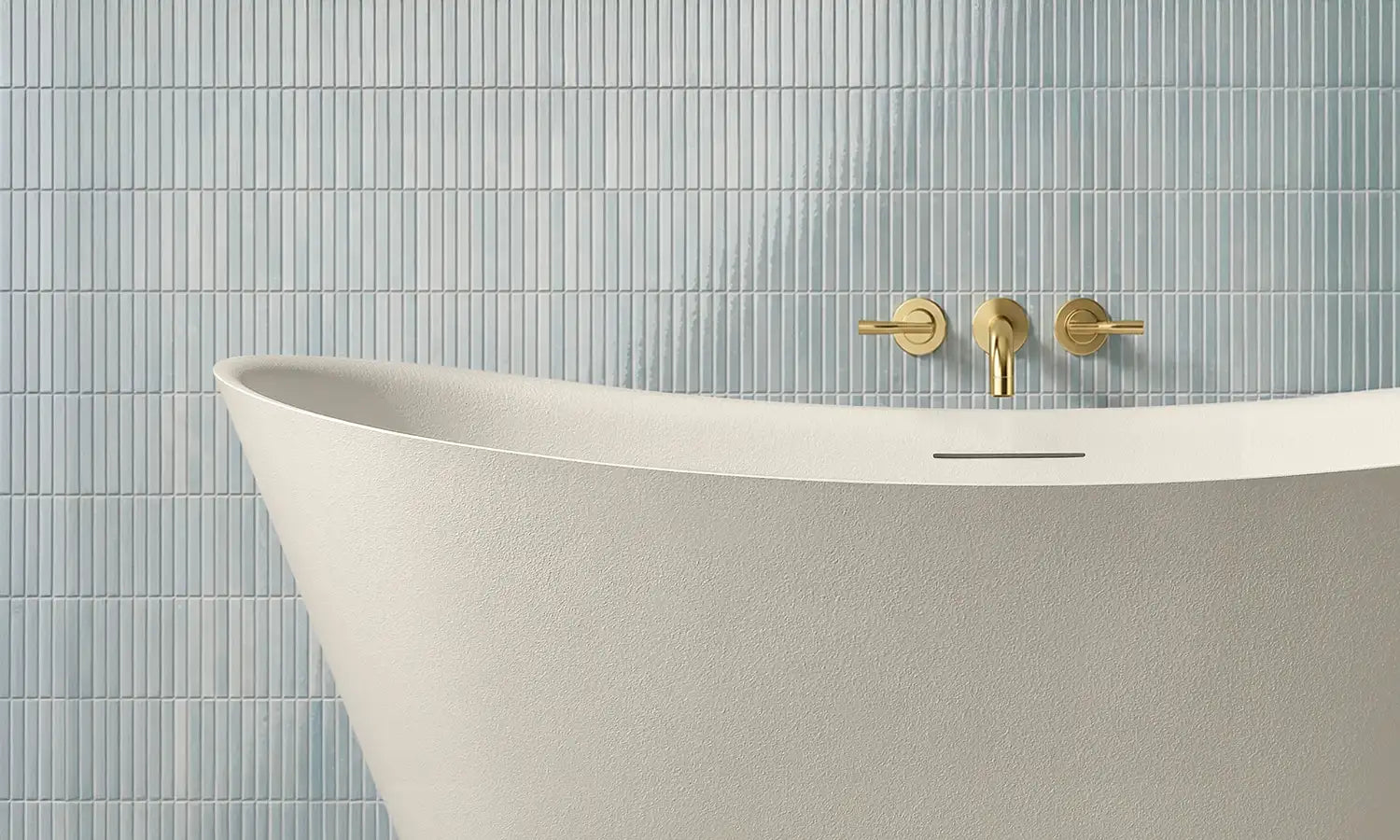 White freestanding ARCHA bathtub with gold faucet against a tiled bathroom wall.